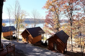 Un hilera de cabañas de madera con techos de metal, frente a un paisaje otoñal y un lago.