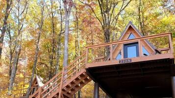 A wooden cabin with a staircase leading up to it, surrounded by trees with autumn foliage.