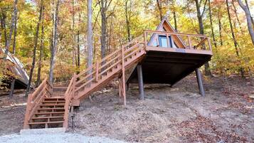 A wooden cabin with a staircase leading to a deck, surrounded by trees.