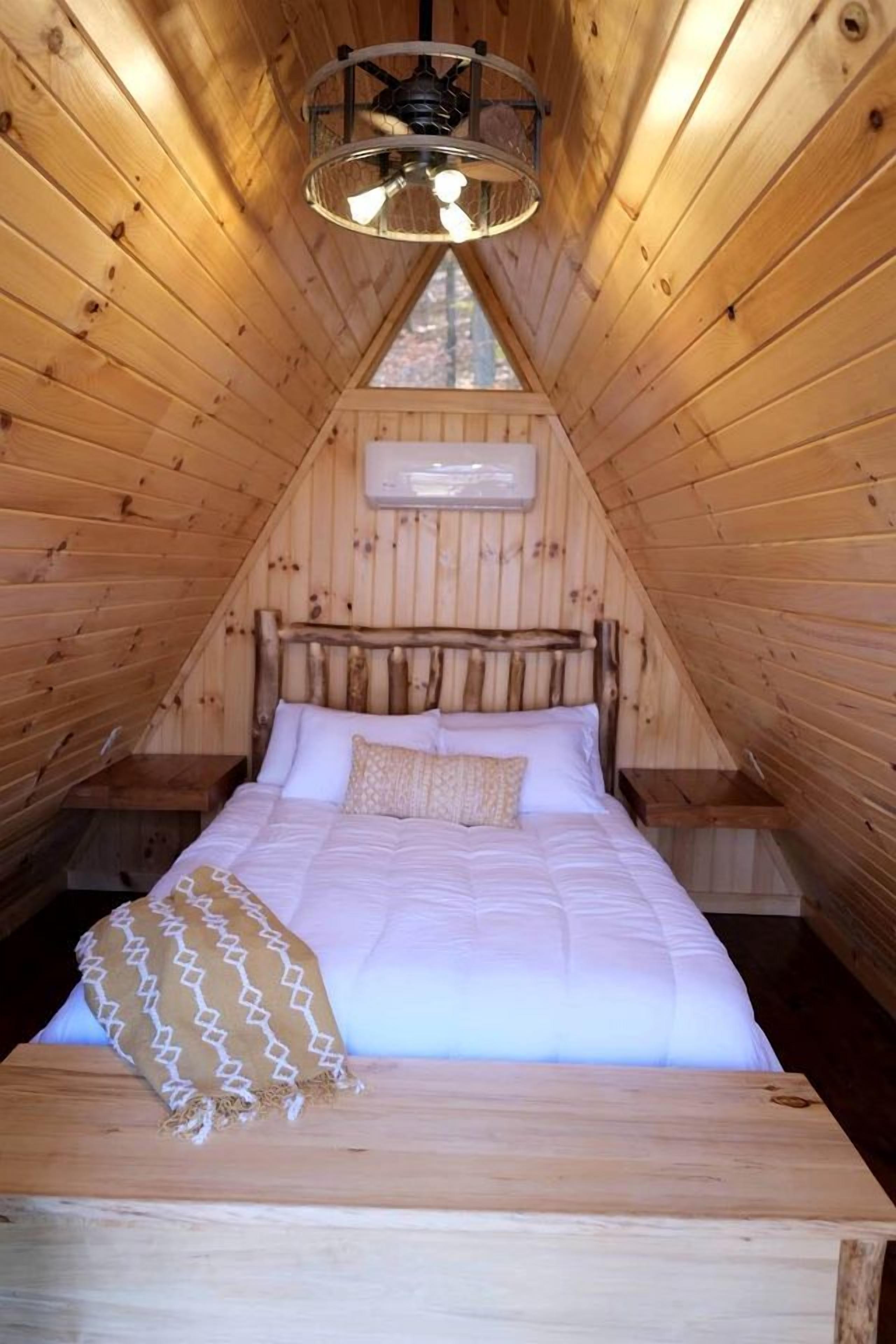 Een houten interieur met een bed, een plafondventilator en een raam.