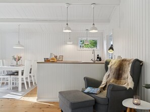 Una cocina moderna con armarios blancos, iluminación colgante, una isla central y una zona de estar acogedora con un plaid de piel.