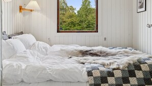 A bedroom with a large window, white walls, a bed with white and gray bedding, a checkered blanket, and a wall-mounted lamp. - "Baarde" - 1.2km from the sea by Interhome (Vejby)