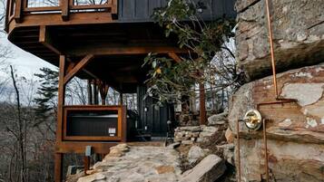 A cabin with a stone staircase leading to a wooden deck and a large window.