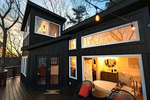 A modern two-story house with a deck, a bathroom with a bathtub, and a dining area with chairs.