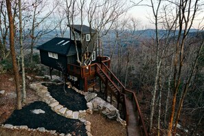 A treehouse with a wooden deck and a staircase leading up to it. - Breathtaking Tree House with Jacuzzi and Lofted Interior in Georgia (Rising Fawn)