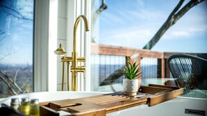 Une cuisine moderne dotée d’une grande fenêtre, d’un robinet doré et d’un plateau en bois sur lequel est posée une plante en pot.