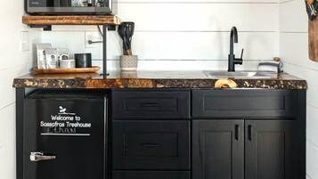 Una cocina compacta con microondas integrado, un lavamanos y un armario negro con un cartel que dice 'Welcome to Sassafras Treehouse'.