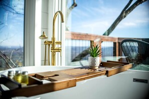 A modern kitchen with a large window, a gold faucet, and a wooden tray with a potted plant. - Breathtaking Tree House with Jacuzzi and Lofted Interior in Georgia (Rising Fawn)