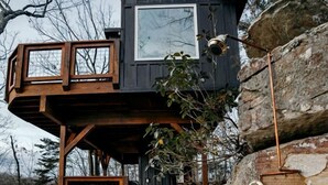 Une cabane avec un escalier en pierre menant à une terrasse en bois et une grande fenêtre.
