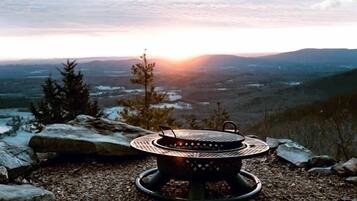 A portable grill on a rocky surface with a view of a sunset over a mountainous landscape.