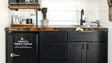 A compact kitchen with a built-in microwave, a sink, and a black cabinet with a 'Welcome to Sassafras Treehouse' sign.
