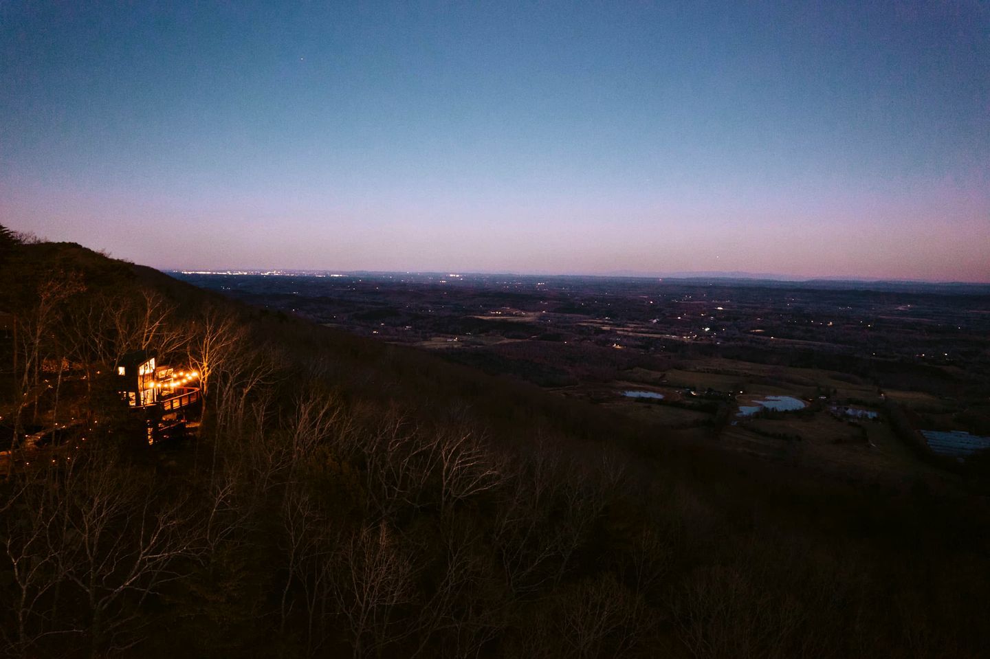 Vista de um vale com uma estrutura iluminada no alto de uma colina.