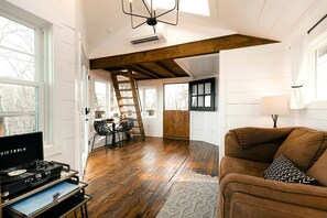 A spacious living area with a wooden floor, a loft-style ceiling, a dining area with chairs, and a brown sofa.