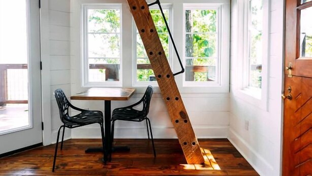 Une pièce avec un plafond en bois, une table entourée de chaises et de grandes fenêtres.