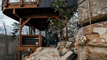 Una cabaña con una escalera de piedra que lleva a una terraza de madera y un ventanal grande.