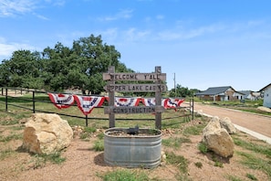 A welcome sign for Upper Lake Cabins with a construction banner and a metal barrel. - Elegant Modern A-Frame Surrounded by Nature in Texas (New Braunfels)