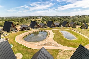A modern resort with unique triangular buildings, a central pond, and a well-maintained lawn. - Elegant Modern A-Frame Surrounded by Nature in Texas (New Braunfels)