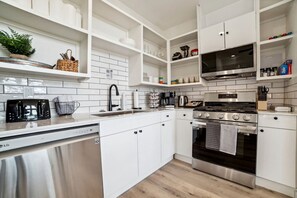 Une cuisine moderne avec des meubles blancs, des appareils en acier inoxydable et un dosseret carrelé.