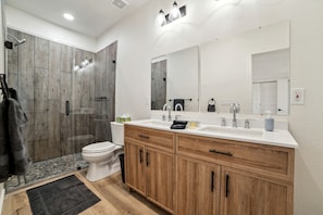 A modern bathroom with a shower, toilet, vanity, and large mirrors. - Elegant Modern A-Frame Surrounded by Nature in Texas (New Braunfels)