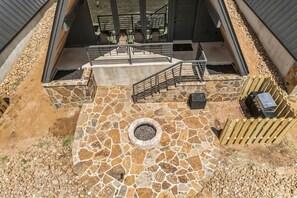 Une terrasse en pierre avec un foyer, des sièges d’extérieur et un escalier menant à un niveau supérieur.