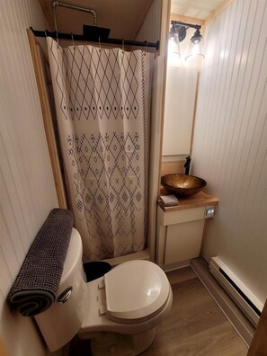 Un baño pequeño con inodoro, lavamanos de madera, cortina de ducha estampada y una toalla en el suelo.