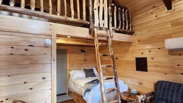 A cabin interior with a loft bed, a ladder, a sofa, and a wooden ceiling.