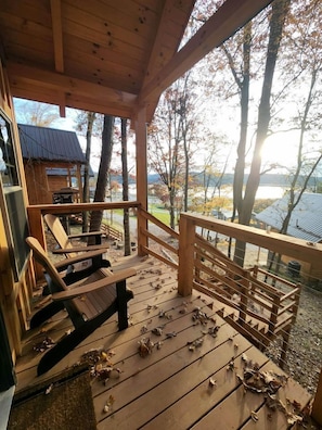 A wooden deck with chairs, a railing, and a view of trees and a building in the background.