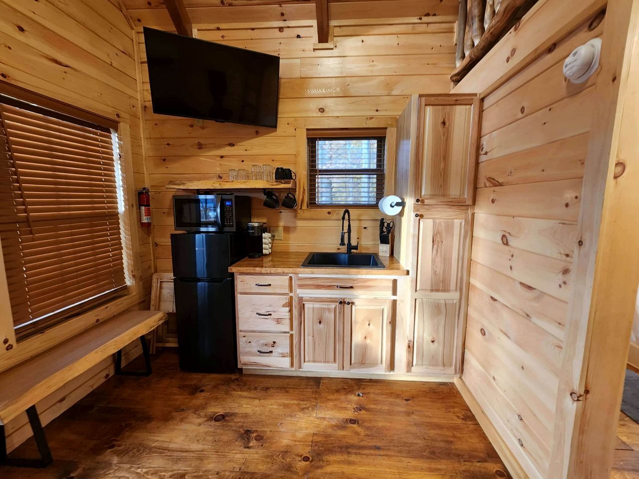 A compact kitchen with wooden cabinets, a black refrigerator, a microwave, and a sink.