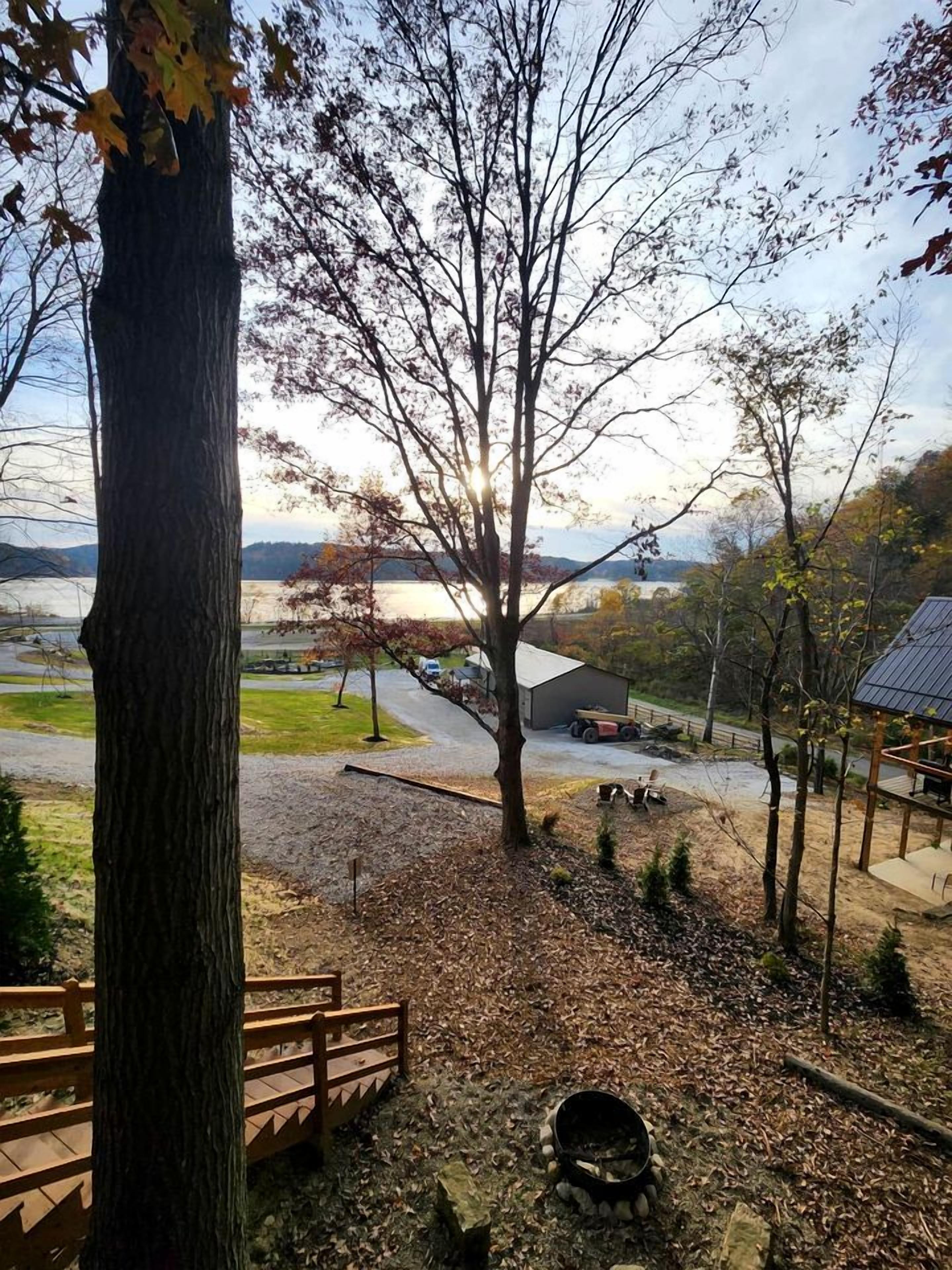 Vue d’une zone au bord du lac, avec une terrasse en bois, un foyer en pierre et un bâtiment en arrière-plan.