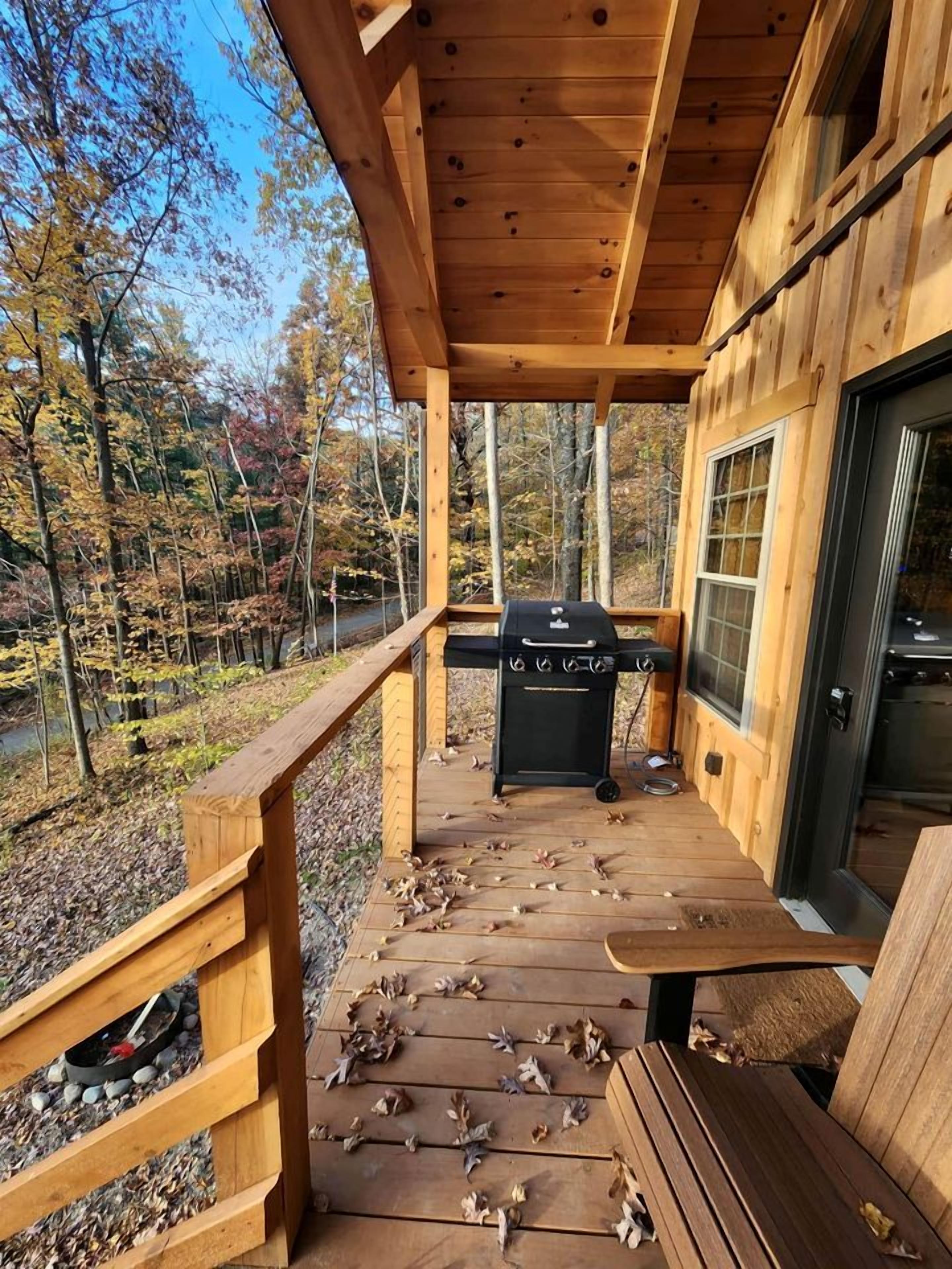 A wooden deck with a grill and a table, surrounded by trees.