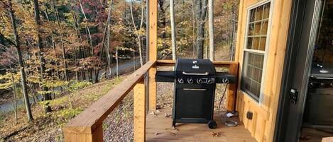 A wooden deck with a grill and a table, surrounded by trees.