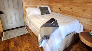 A wooden cabin bedroom with a bed, a nightstand, a door, and a wooden floor.