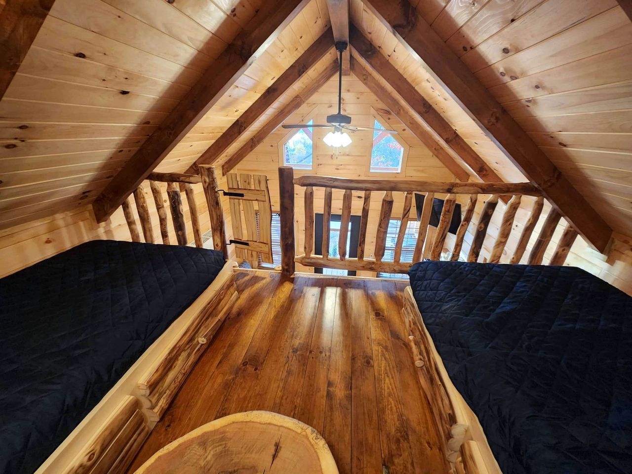 Une chambre mansardée en bois, avec un plafond en pente, une poutre centrale en bois et une fenêtre donnant sur les arbres.