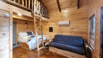 A wooden cabin interior with a loft bedroom, a sofa, a ladder, and a window.