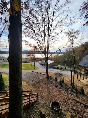 Vue d’une zone au bord du lac, avec une terrasse en bois, un foyer en pierre et un bâtiment en arrière-plan.