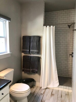 A bathroom with a toilet, a bidet, a shower curtain, and towels hanging on the wall. - Charming Cabin for Glamping Vacations in Wimberley, Texas (Wimberley)