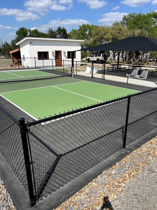 A tennis court with a fence, a small building, and a covered seating area.
