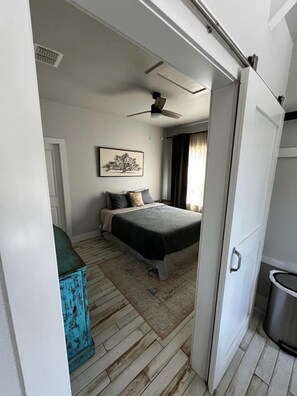 A bedroom with a bed, a ceiling fan, a window with curtains, and a door.