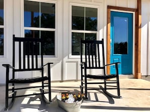 Two black chairs outside a building with a blue door, and a bucket with bottles on the ground.