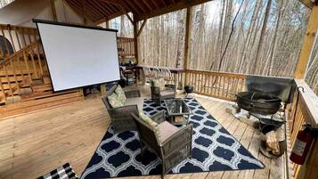Une terrasse couverte, aménagée avec du mobilier d’extérieur, un barbecue et un écran de projection.