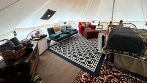 A tent with a bed, a sofa, a red chair, a small table, and a patterned rug.