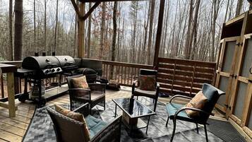 Une terrasse extérieure avec un barbecue, des meubles en osier et une vue sur une forêt.