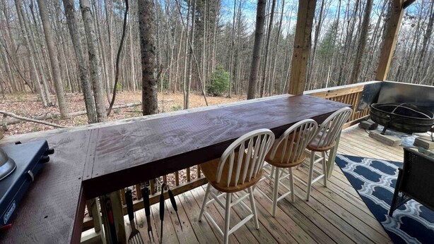 A wooden deck with a long table and four chairs, a grill, and a TV.