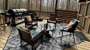 An outdoor deck with a grill, wicker furniture, and a view of a forest.