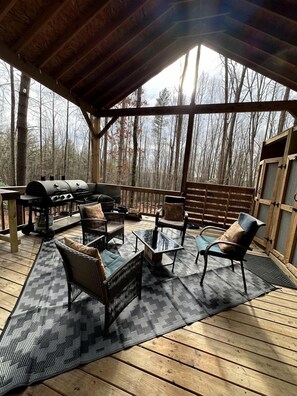 Una terraza al aire libre con una parrilla, mobiliario de mimbre y vistas a un bosque.