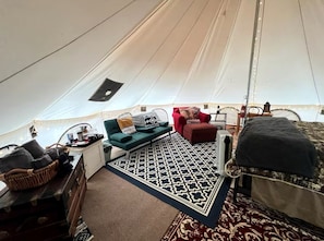 A tent with a bed, a sofa, a red chair, a small table, and a patterned rug.