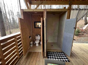 A wooden deck with a wooden door leading to a small enclosed bathroom with a toilet and shower area. - Magical Glamping Tent in the Woods near Stone Mountain State Park, North Carolina (Wilkes County)