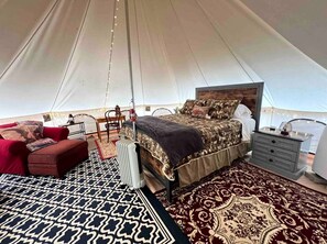A tented accommodation with a bed, a red sofa, a bedside table, and a patterned rug.