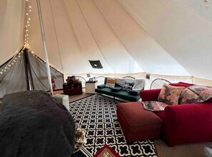 A tent interior with a patterned rug, a red sofa, and a small table with a lamp.
