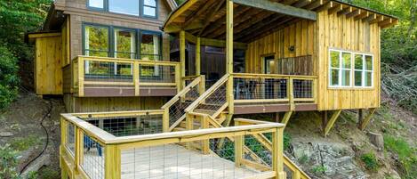 A wooden cabin with a balcony and a deck, surrounded by trees.